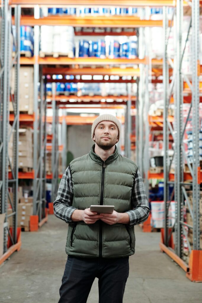 pexels photo 4484077 4484077 Warehouse worker stands in aisle using a tablet to manage inventory.